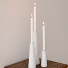 Three white candles in textured candle holders on a wooden surface with a plain background