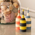 Three colorful striped toothpick dispensers on a reflective surface with a jar of seashells in the background.