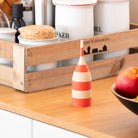 Red and white striped toothpick dispensers on a wooden shelf with a bowl of fruit and a wooden crate in the background.