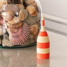 Decorative striped toothpick dispenser with a jar of shells in the background